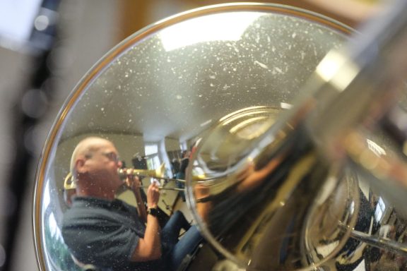 Ein Musiker spielt Trompete, sein Bild spiegelt sich in einem glänzenden Instrument.