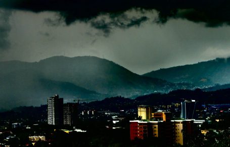 Dunkle Wolken über Stadtlandschaft und hügeligem Hintergrund.