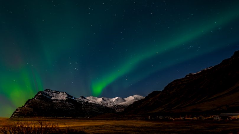 Grüne Nordlichter über einer Berglandschaft bei Nacht.