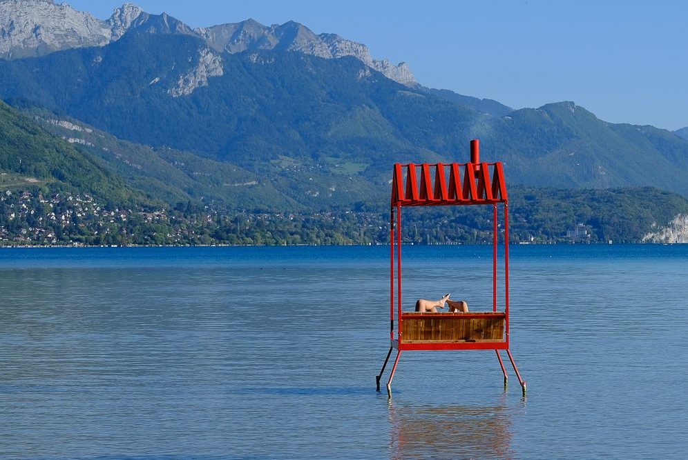 Rote Holzstruktur auf Wasser mit Bergen im Hintergrund und klarem Himmel.