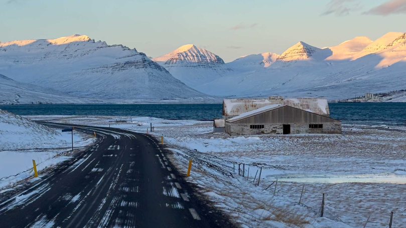 Berglandschaft mit schneebedeckten Gipfeln und einer verfallenen Hütte am Straßenrand.