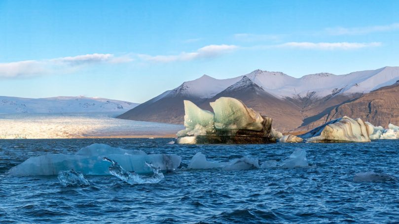 Eisberge schwimmen in einem klaren, blauen Wasser mit Bergen im Hintergrund.